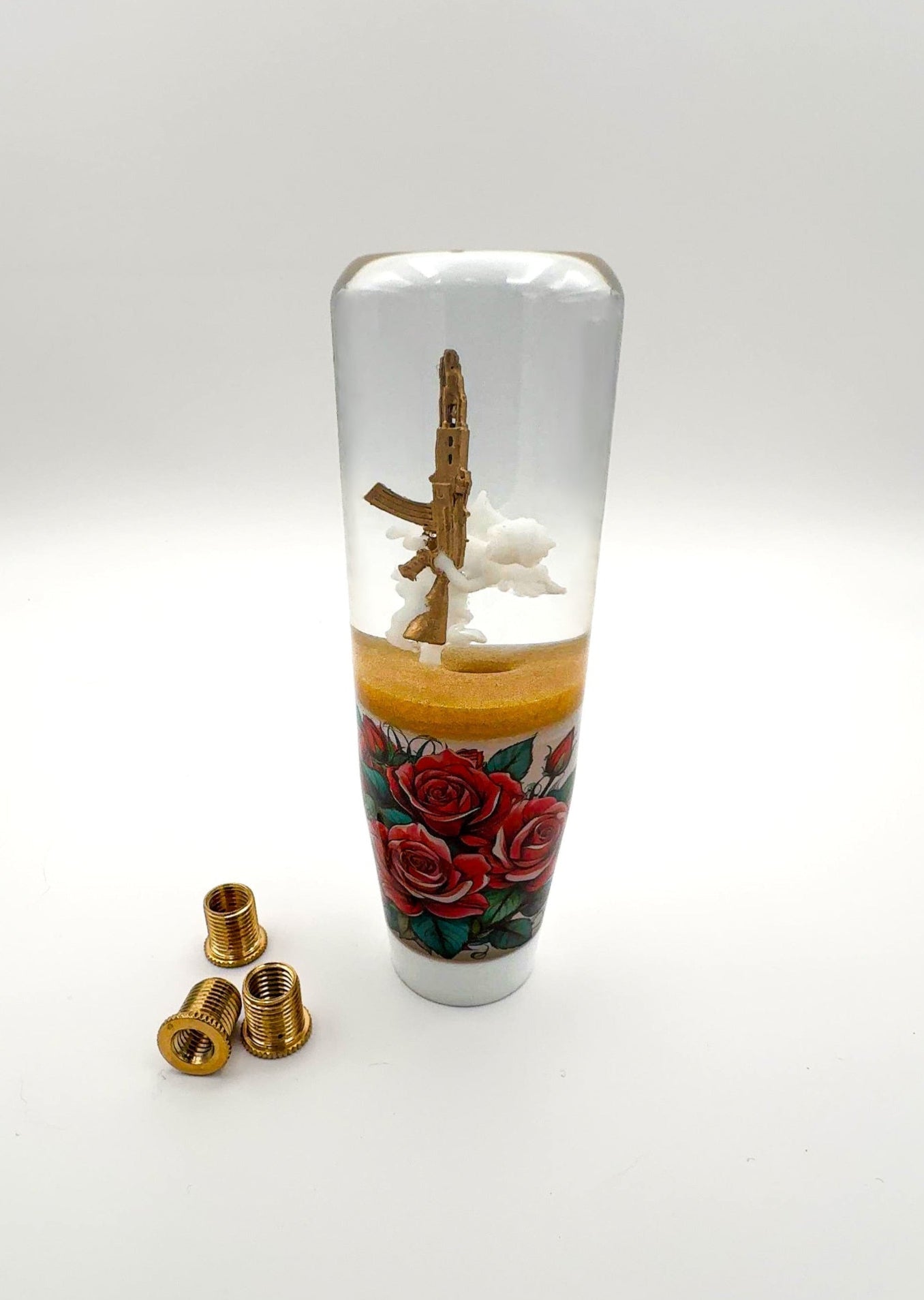 White Cupid shift knob holding a gold AK-47 with red roses and gold trim. Resin-made, weighted, and fits most manual and automatic cars.