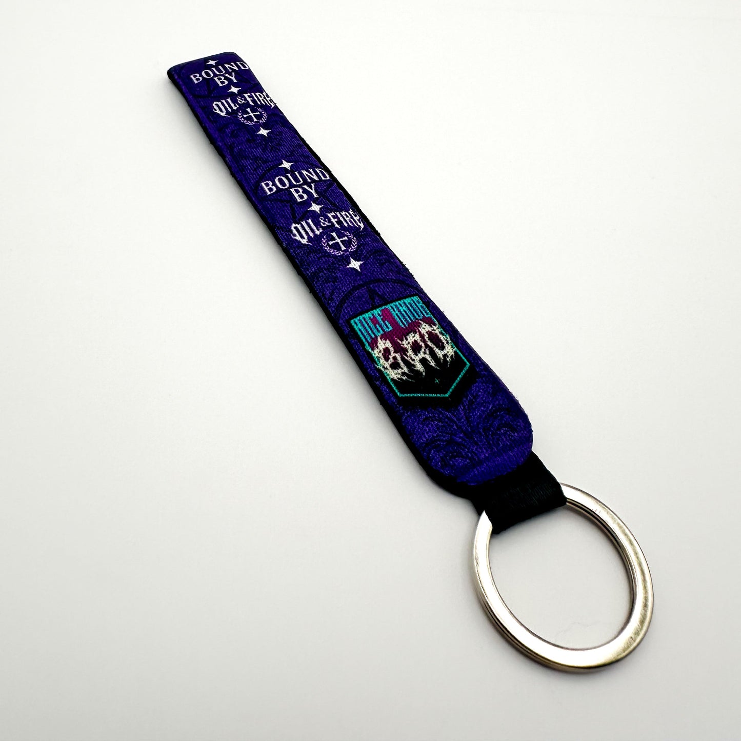 a keychain that is purple black and white that says bound by Oil and fire