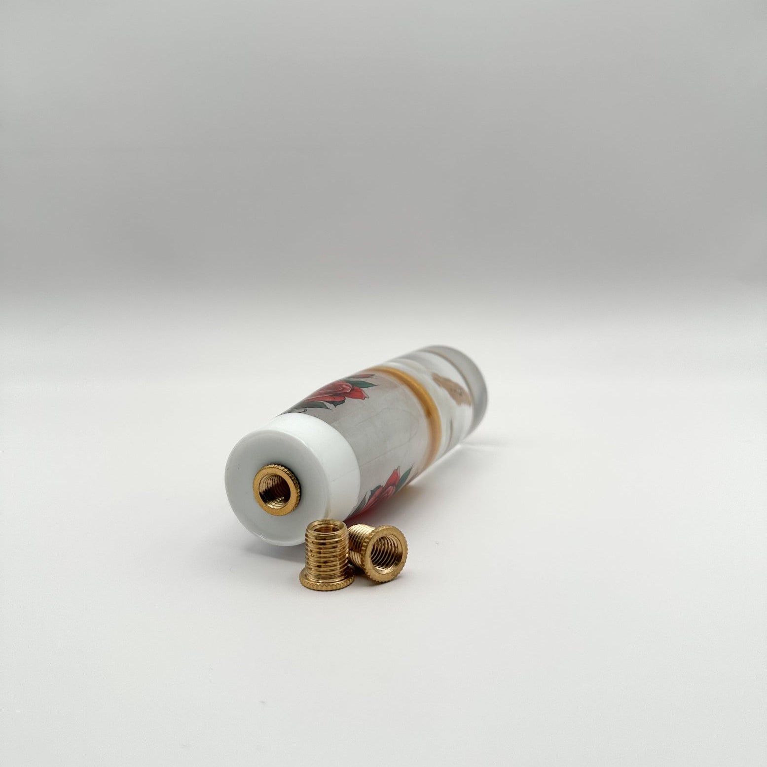 White Cupid shift knob holding a gold AK-47 with red roses and gold trim. Resin-made, weighted, and fits most manual and automatic cars.