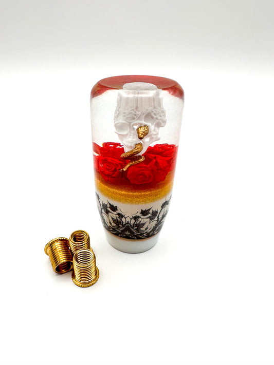 a white skull with a golden snake on a bed of red roses weighted resin shift knob for manual or automatic cars with threaded inserts 